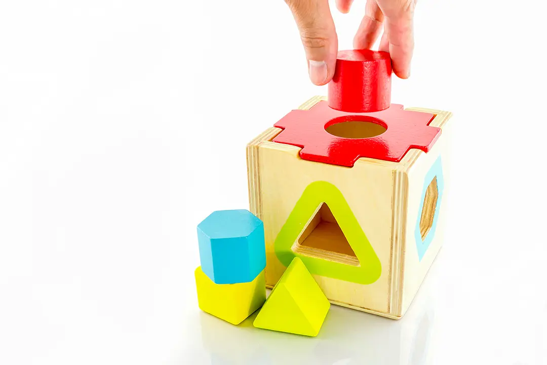 Eine Hand, die einen Zylinder in ein Loch legt, Spiel mit dem Einsetzen von Formen in einen Würfel.