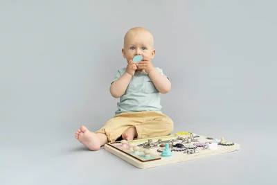 12 Monate altes Baby in einem Hintergrundstudio, das mit einem Montessori Busy Board spielt