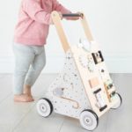 Ein kleines Mädchen spielt mit einem Baby-Schiebe-Lauflernwagen - Multi-Aktivitäten - Pastellfarben.