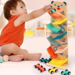 Ein Kleinkind spielt mit einer Holzrampe Votures - Rennbahn für Kleinkinder, indem es die Rampe benutzt, um mit kleinen Autos ein Rennen zu veranstalten.