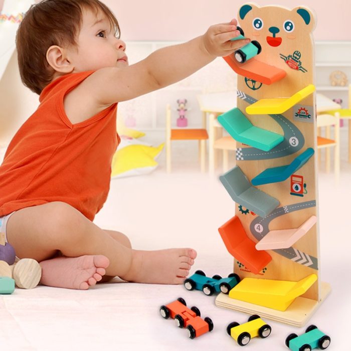 Ein Kleinkind spielt mit einer Holzrampe Votures - Rennbahn für Kleinkinder, indem es die Rampe benutzt, um mit kleinen Autos ein Rennen zu veranstalten.