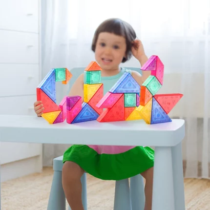 Ein kleines Mädchen sitzt mit einem Magnetischen Tangram an einem Tisch.